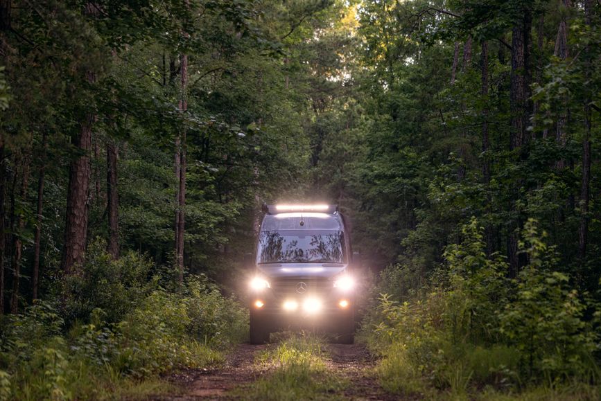 A Tiffin GH2 drives through a wooded area with lights on
