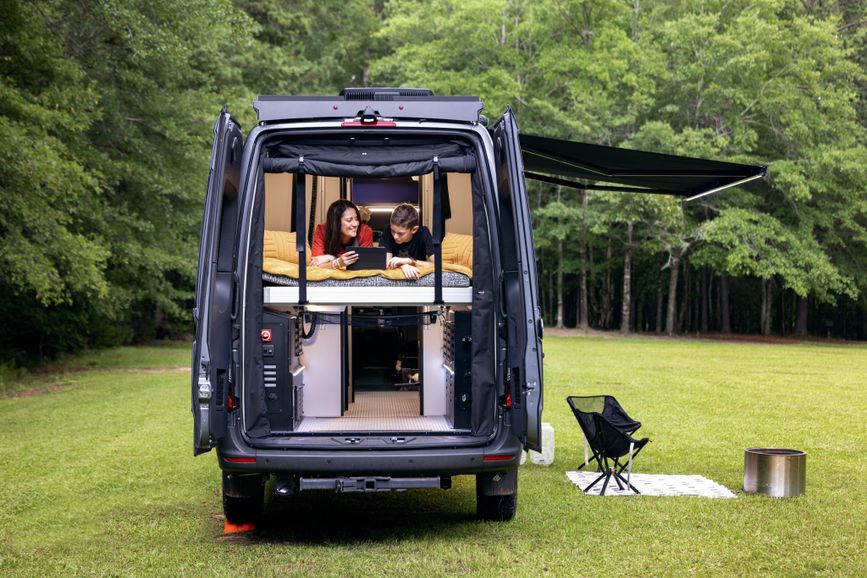 A child and an adult lounge in a Tiffin GH2 parked outside 
