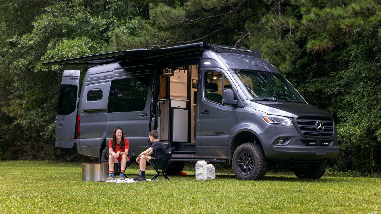 A child and an adult sit outside a 2026 Tiffin GH2 on a sunny day