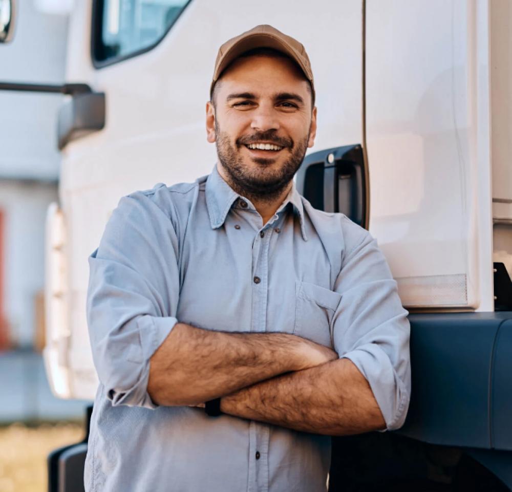 A smiling man in a light-blue button-up and hat leaning against a white truck